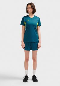 Turkos sporttröja och shorts med gula detaljer, utrustad med V-ringning och logotyp på vänster bröst, tillverkad av lättviktsmaterial.