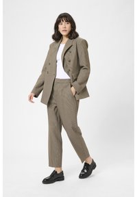Bruin geruit pak met een dubbelzijdige blazer en bijpassende broek. Bevat een gestructureerde stof en zwarte schoenen. Casual witte top eronder.