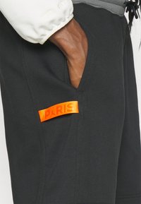 Black shorts featuring an orange "PARIS" label, made from soft fabric with a relaxed fit and side pocket detail.