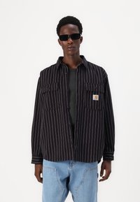 Black and white striped shirt with two front pockets, button-down design, relaxed fit, paired with light blue jeans.