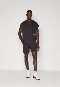 T-shirt atlética preta com ajuste solto e mangas curtas, combinada com calções pretos a condizer. Detalhe do logótipo Puma em branco. Ténis brancos e vermelhos.