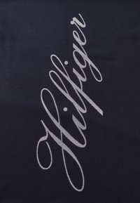 Tela azul marino con una textura suave que presenta letras grandes y en cursiva de color plateado "Hilfiger" destacándose en diagonal a lo largo de la superficie.