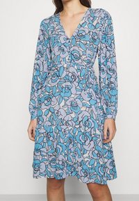 Blaues Blumenkleid mit V-Ausschnitt, langen Ärmeln und tailliertem Schnitt. Aus leichtem Stoff mit einem Muster aus Rosen und Blättern.