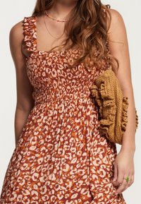 Robe à imprimé léopard marron et crème avec corsage smocké et bretelles volantées ; associée à un sac à main texturé marron.