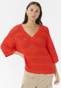 Pulover roșu tricotat cu decolteu în V, având un model cu țesătură deschisă și mâneci scurte. Textura este ușoară și respirabilă.