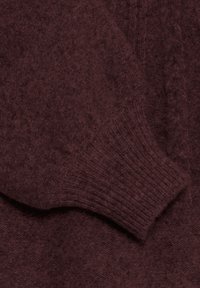 Maglione lavorato a maglia color bordeaux con polsini a costine, texture morbida e dettagli a trecce lungo il corpo per un maggiore interesse visivo.