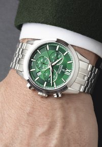 Montre chronographe en acier inoxydable argenté avec un cadran vert, trois sous-cadrans, des aiguilles lumineuses et une fenêtre de date à 6 heures.