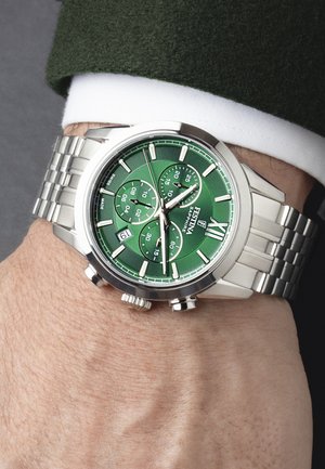 Montre chronographe en acier inoxydable argenté avec un cadran vert, trois sous-cadrans, des aiguilles lumineuses et une fenêtre de date à 6 heures.