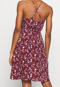 Burgundské květinové šaty s přiléhavým pasem, křížovými ramínky a rozšířenou sukni. Mají malé květiny v růžové, modré a bílé barvě.