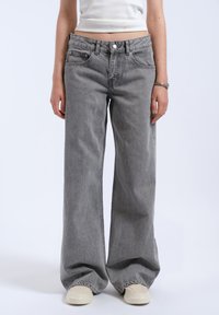 Jean large gris avec une taille haute, dotée d'une fermeture à bouton, de poches avant et d'un tissu en denim doux et légèrement texturé.