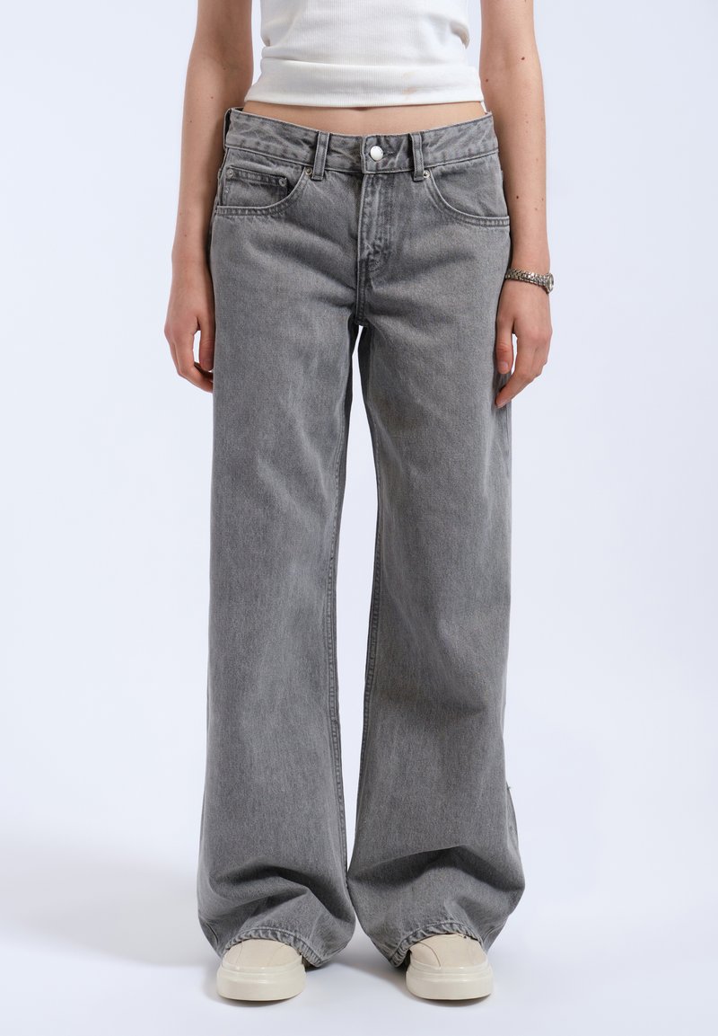 Jean large gris avec une taille haute, dotée d'une fermeture à bouton, de poches avant et d'un tissu en denim doux et légèrement texturé.