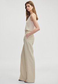 Beige, wijde pantalon gemaakt van lichte stof, met frontzakken en een hoge taille, gecombineerd met een aansluitend beige tanktop.