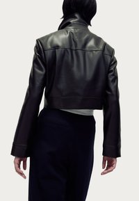 Taillierte schwarze Lederjacke mit matter Oberfläche, breitem Kragen und langen Ärmeln. Das Modell zeigt die Rückansicht; kombiniert mit dunklen Hosen.