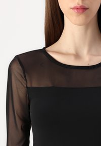 Černý top s dlouhým rukávem, který má průhledný černý síťovaný výstřih a rukávy, tělo je solidní černé, kulatý výstřih, hladká textura a přiléhavý střih.