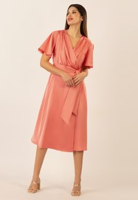 Korallefarbene Satin-Wickelkleid mit kurzen, flatternden Ärmeln, einem V-Ausschnitt und einem Taillengürtel. Der Rock ist knielang und hat einen leichten Glanz.