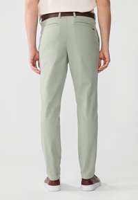 Pantalon léger vert pour homme en mélange de coton, design droit, avec deux poches arrière et une texture lisse. Associé à des baskets marron.