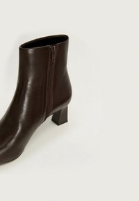 Bruine leren enkelboot met een vierkante hak, voorzien van een zijrits en een gladde textuur, wat zorgt voor een stijlvolle en moderne uitstraling.