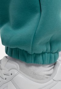 Teal joggerbroeken met een ribbelsmanchette bij de enkel, gecombineerd met een witte sneaker met een gestructureerd oppervlak en veters.