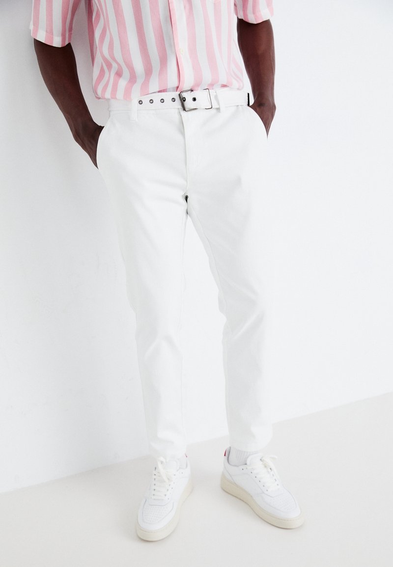 Vita bomullsbyxor med slim fit, i kombination med en rosa randig kortärmad skjorta och vita sneakers. Slät textur, enkel design.