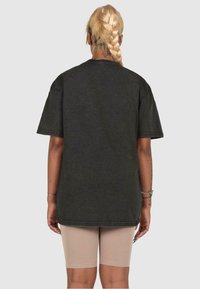 Schwarzes, übergroßes T-Shirt mit kurzen Ärmeln, aus Baumwolle und mit geradem Saum. Kombiniert mit beigen Radlerhosen. Die Haare sind geflochten.