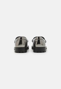 Fémes ezüst slip-on cipők fekete gumitalppal. Sima felszín, kerek orral és minimális varrási részletekkel.