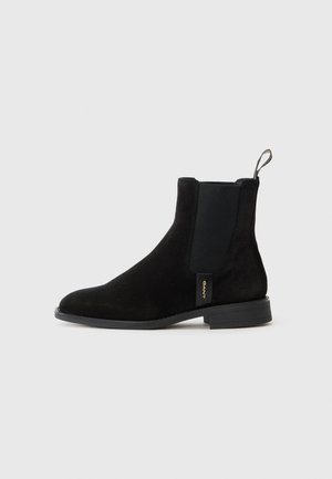 Black suede chelsea boot with elastic side panels, rounded toe, and a small heel. Features a pull tab on the back and logo detail on the side.