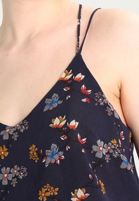Floral-patterned navy fabric top with thin straps, featuring multicolored flowers and leaves. Lightweight, flowing design with a V-neckline.