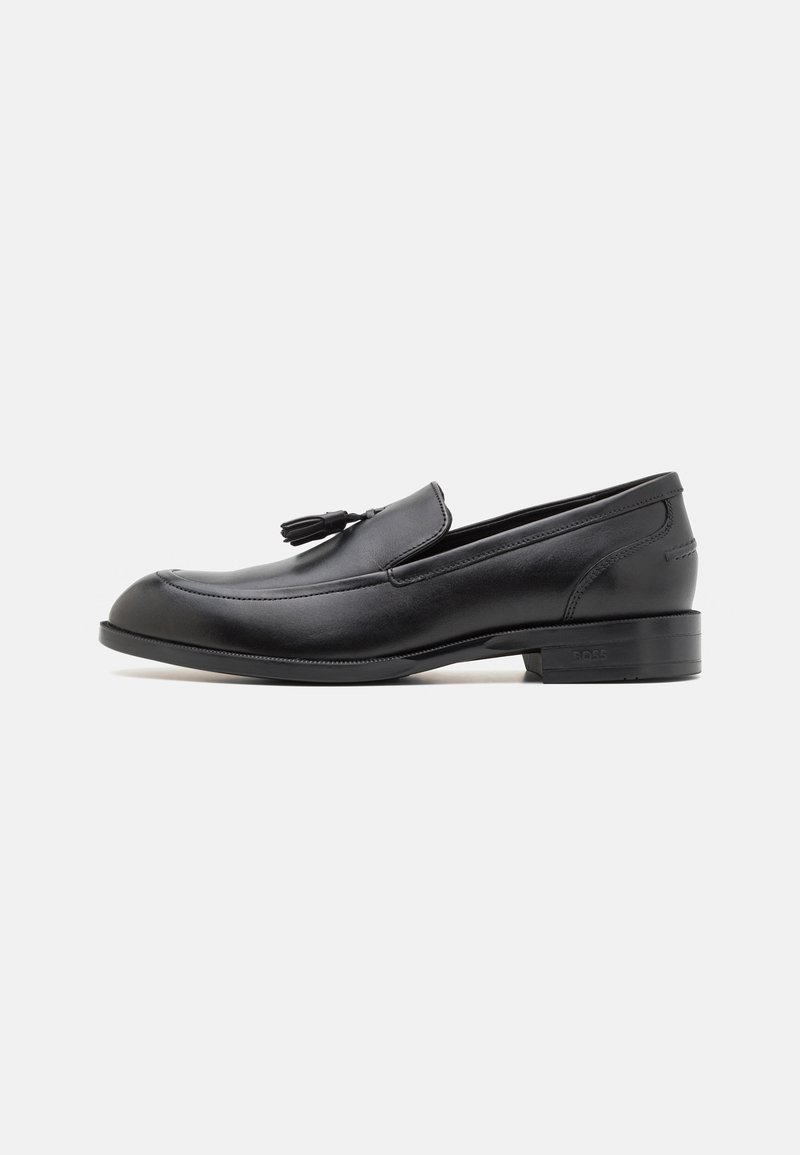 Mocasines de cuero negro con superficie lisa, punta redondeada y detalle de borlas en el empeine. Tacón bajo apilado y costuras a tono.