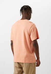 T-shirt à col rond à manches courtes en coton pêche doux, avec une coupe décontractée et des détails de couture minimalistes, porté avec un pantalon beige.