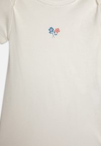 Kratki rukavi kremasti bodi od mekanog pamuka, s jednostavnim printanim dizajnom plavih i ružičastih cvjetova na prsima.