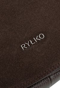Brown suede surface with a smooth texture, featuring silver embossed "RYŁKO" logo and fine stitching detail along the edges.