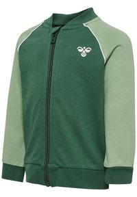 Veste zippée verte avec des manches vert clair contrastantes, dotée d'un col haut, de poignets côtelés et d'un logo d'abeille sur la poitrine.