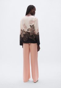 Haut fluide à manches longues couleur crème avec broderie florale, associé à un pantalon rose à jambes larges. Présente un col rond et un ourlet noir contrastant.