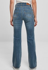 Faded blue denim flared jeans with a high waist, featuring two back pockets and a leather patch at the waistband.