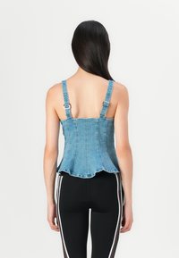 Denim peplum top with adjustable straps, light blue color, featuring a fitted bodice and flared hemline. Comes with silver hardware accents.