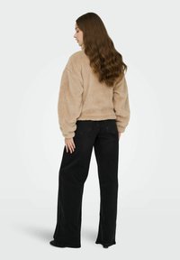 Pull beige duveteux à manches longues associé à un jean noir taille haute à jambes larges, vu de dos, mettant en valeur les textures et les formes.