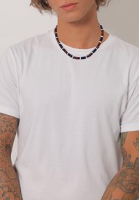 Weißes T-Shirt mit kurzen Ärmeln und rundem Ausschnitt, getragen mit einer mehrfarbigen Perlenkette, die dunkle und helle Perlen in verschiedenen Größen aufweist.
