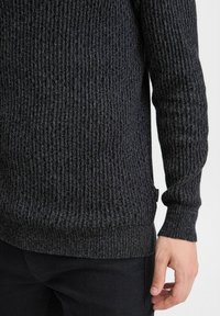Dunkelgrauer gerippter Strickpullover mit langen Ärmeln, strukturiertem Stoff und einem körpernahen Saum. Verfügt über ein kleines Etikett auf der unteren linken Seite.