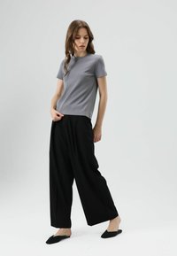 Grijs T-shirt met korte mouwen en een ronde hals, gecombineerd met wijde zwarte broek en zwarte platte slippers. Soepele textuur, minimalistisch design.