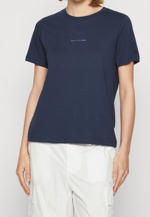 Vrouw draagt een navyblauw T-shirt met korte mouwen met de tekst “Marc O’Polo DENIM”, gecombineerd met witte cargobroek.