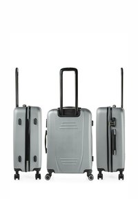 Maleta rígida plateada con asa telescópica negra, textura lisa, cuatro ruedas y cierre de cremallera. Presenta ranuras horizontales en la parte frontal.