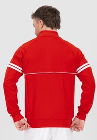 Rote Sportjacke mit langen Ärmeln, weißen Streifenakzenten an den Schultern, hohem Kragen und enger Passform. Glattes Stoffmaterial in einfarbiger Ausführung.