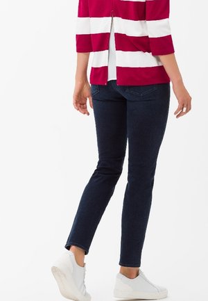 Haut rayé rouge et blanc avec une fente au dos, associé à un jean bleu foncé et des baskets blanches. La tenue présente un design décontracté et ajusté.
