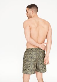 Pánské plavky v olivově zelené barvě s černým květinovým vzorem, elastickým pasem a bočními kapsami. Texturovaná tkanina s volným střihem.