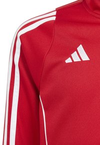 Rode sportjack met witte strepen en stoftextuur, voorzien van een wit logo op de borst en contrasterende witte accenten op de mouwen.