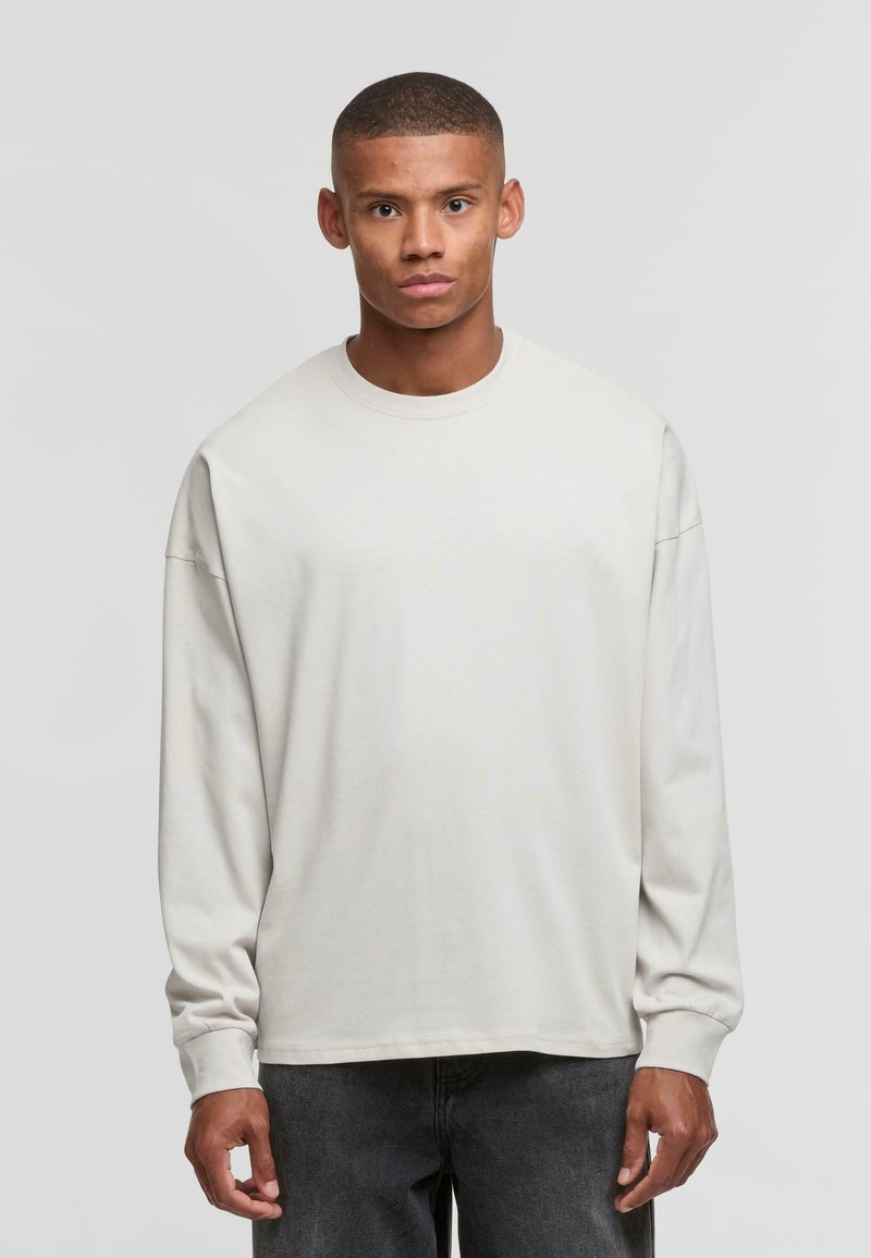 Camiseta de manga larga en gris claro, hecha de algodón suave, con un escote redondo y un corte holgado. Diseño simple, sin patrones ni acentos visibles.