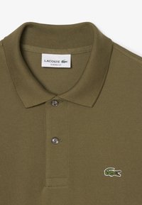 Olivgrünes Poloshirt aus strukturiertem Stoff, mit zwei Knöpfen und einem kleinen gestickten Krokodil-Logo auf der linken Seite. Klassische Passform.