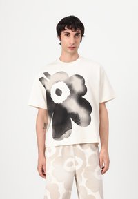 Kortärmad krämfärgad t-shirt med ett stort svart blommönster. Tyget ser mjukt ut med en lös, boxig silhuett som komplementeras av mönstrade byxor.