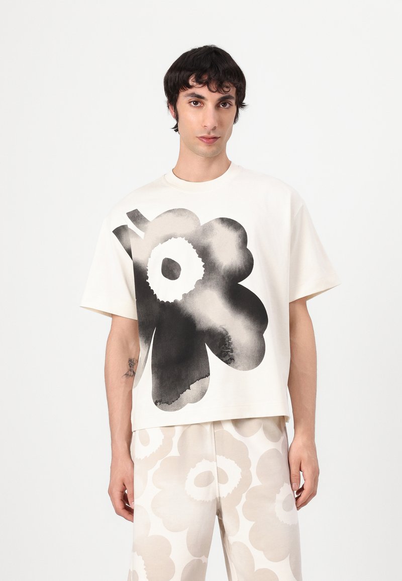 Kortärmad krämfärgad t-shirt med ett stort svart blommönster. Tyget ser mjukt ut med en lös, boxig silhuett som komplementeras av mönstrade byxor.