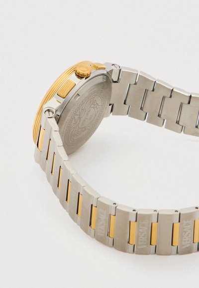 Ασημένιο και χρυσό μεταλλικό ρολόι με υφή στην κάσα και το λουρί, με διακοσμημένη πλάτη και σκάλιστες λογότυπες λεπτομέρειες στα κρίκους.